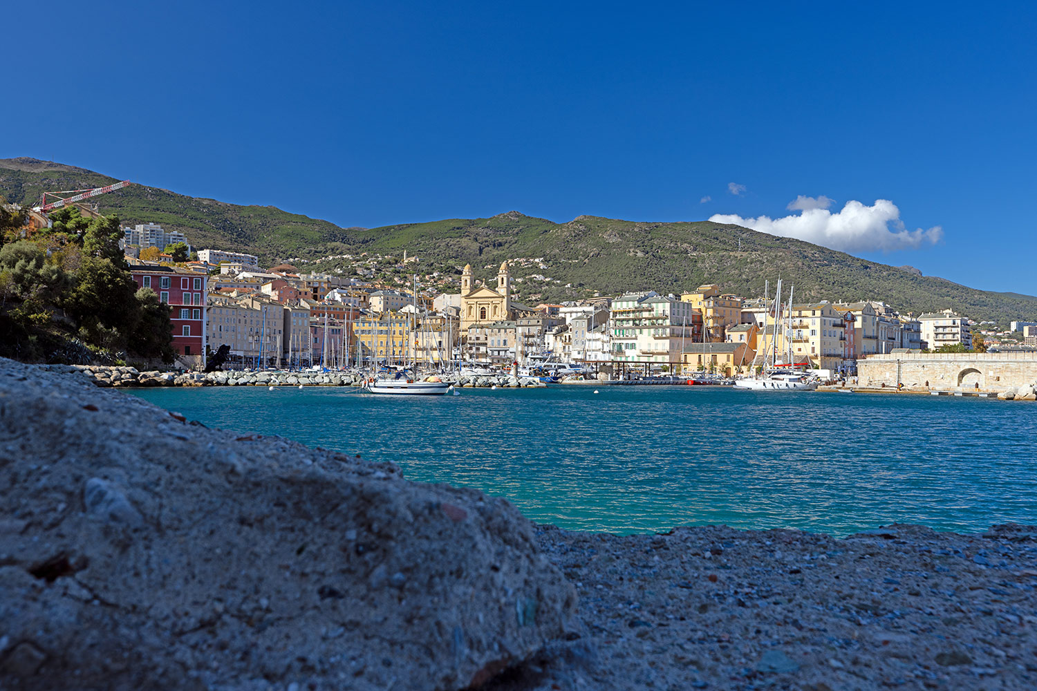 Vue panoramique du port de Bastia et de la promenade historique avec des bâtiments colorés sous un ciel bleu
